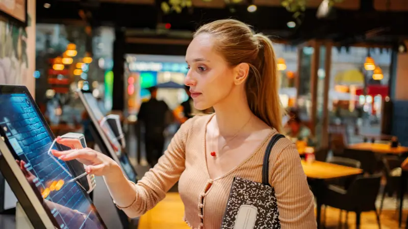 Young woman using self-service kiosk at restaurant